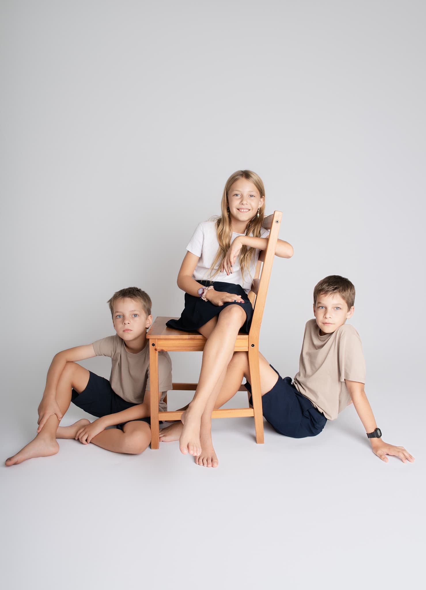 Three siblings in the Brandon studio, a girl seated on a wooden chair with her two brothers on the floor either side